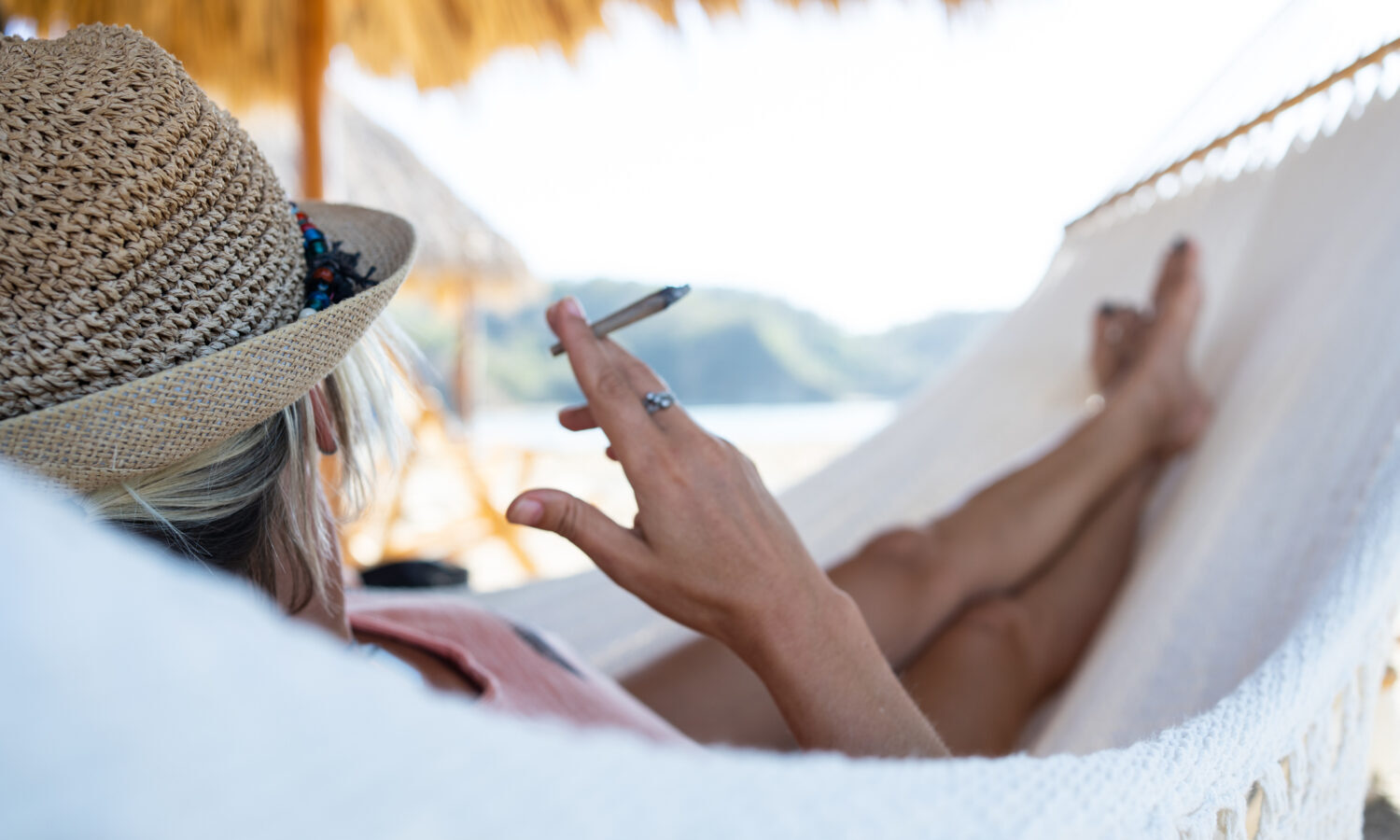 Woman with a wicker hat smoking while lying in a hammock.